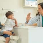 Health-care provider and child reaching to high-five across a desk between them. The child sits on a parent's lap.