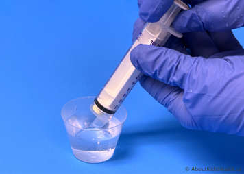 Tip of syringe containing mercaptopurine tablet dipped into a medicine cup of warm water