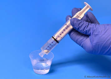 Gloved hand holding syringe with mercaptopurine tablet and 5 mL of warm water in it