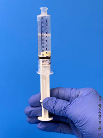 Gloved hand holding oral syringe containing mercaptopurine tablet, 5 mL of water and 5 mL of air