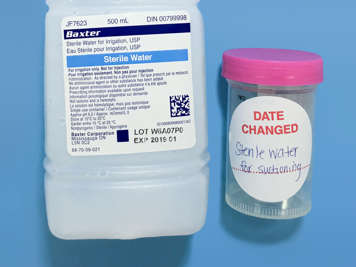 A sterile water bottle and a labelled cup of sterile water for suctioning.