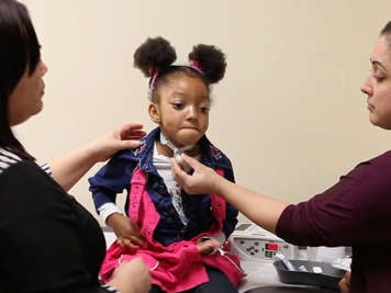 Two people helping a child with a tracheostomy