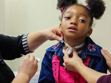 Caregivers detaching tracheostomy tube ties on child.