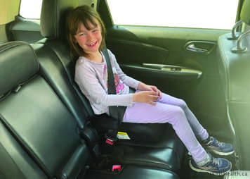 school-age child sitting in booster seat with seatbelt on