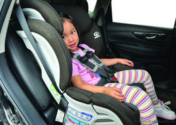 child in a forward facing car seat with straps done up