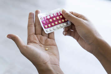 Hand holding birth control packet and other hand holding pill