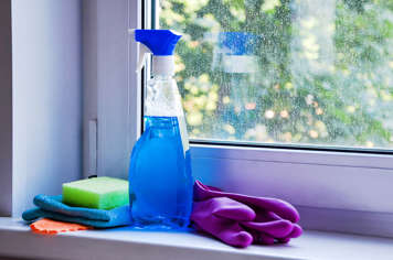 Spray bottle of glass cleaner next to dirty window