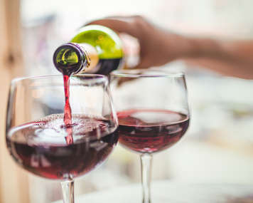 Person pouring two glasses of red wine