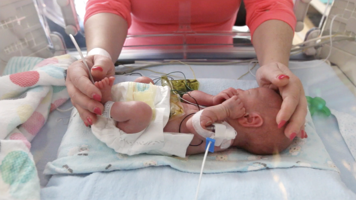 An infant whose feet and head are being cupped by a woman