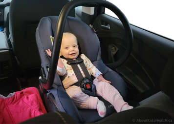baby in rear-facing bucket car seat with straps secured and car seat handle up