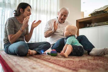 Mother and grandfather clapping and playing with baby on the floor