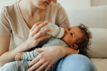 Woman holding baby on her lap and feeding the baby a bottle