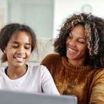 Woman and teen girl smiling and sitting beside each other in front of a laptop