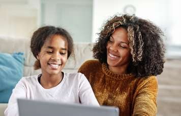 Woman and teen girl smiling and sitting beside each other in front of a laptop