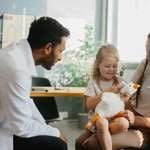 Child sitting on parent's lap across from a health-care provider who leans forward to talk to the child