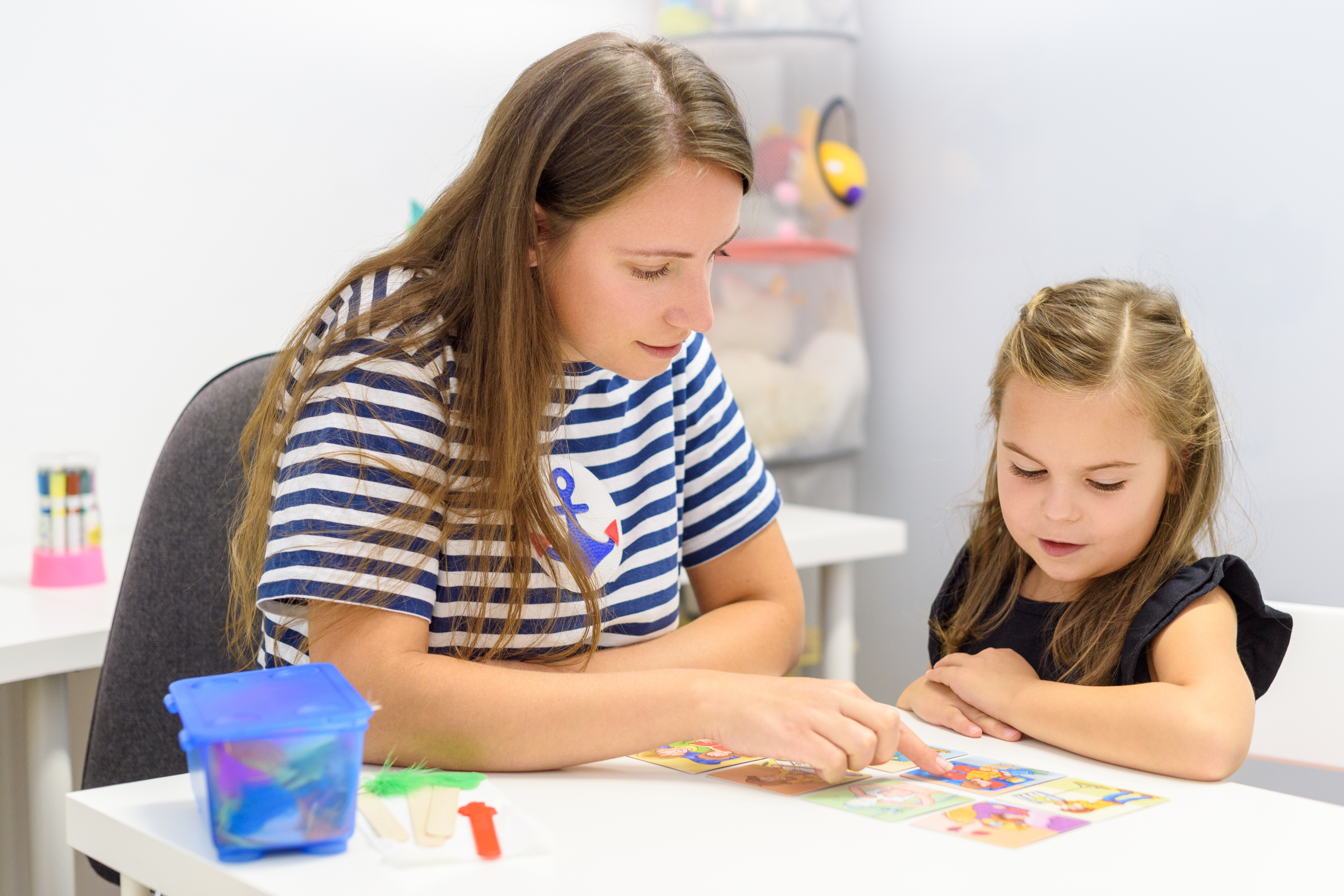 Child and speech-language pathologist sitting at a small table looking at a picture together