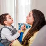 Toddler sitting on woman's lap on a couch. They are facing each other and have their chins tilted up slightly