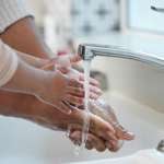Closeup on hands of an adult and small child washing their hands at a sink with water running from the faucet