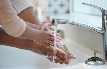Closeup on hands of an adult and small child washing their hands at a sink with water running from the faucet