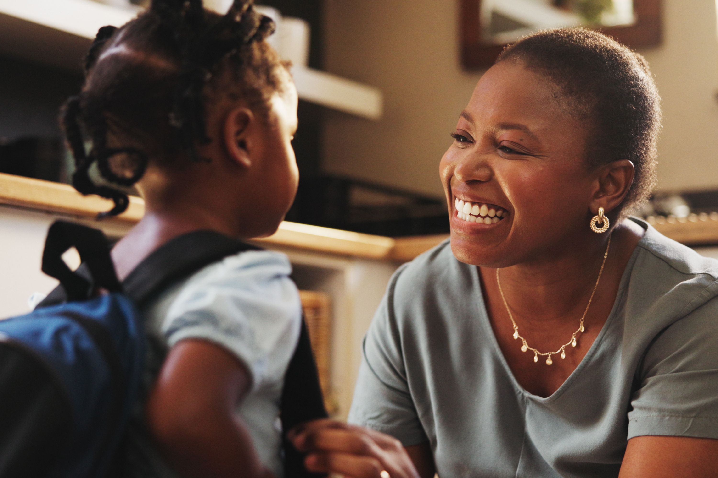Woman and child in a kitchen. The woman crouches to be at eye level with the child and is smiling at her