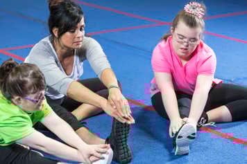 An adult is stretching with two youth who have Down syndrome