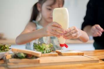 Child squeezing mayonnaise onto a sandwich