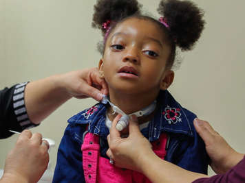 Helper holds the child’s shoulder and tracheostomy while the main person removes the tracheostomy ties